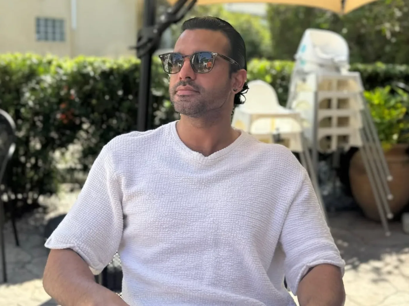 Flowaver in sunglasses and a white knit shirt, sitting outside on a sunny patio