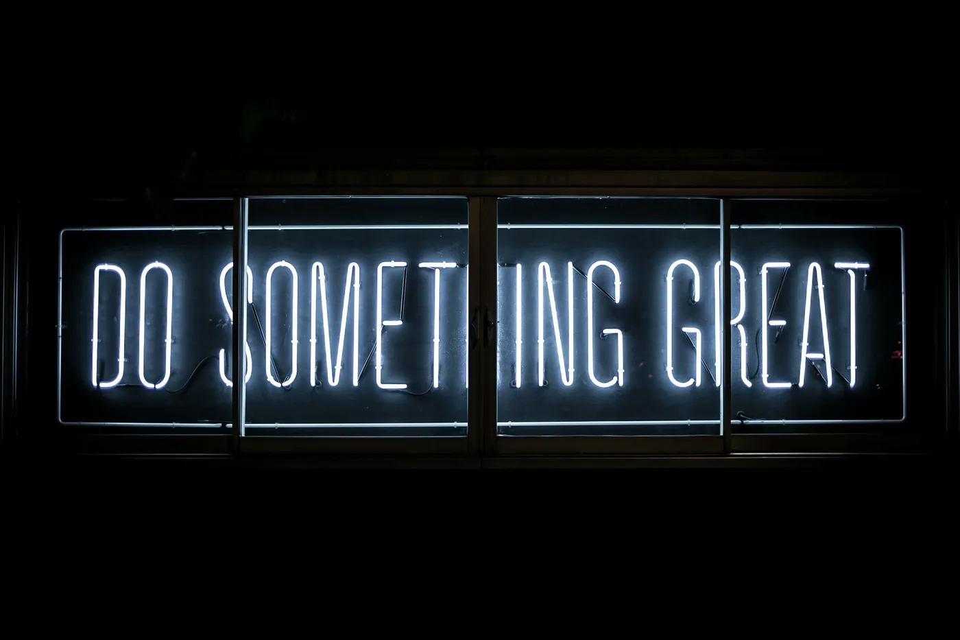 Neon sign reading "do something great" against a dark wall