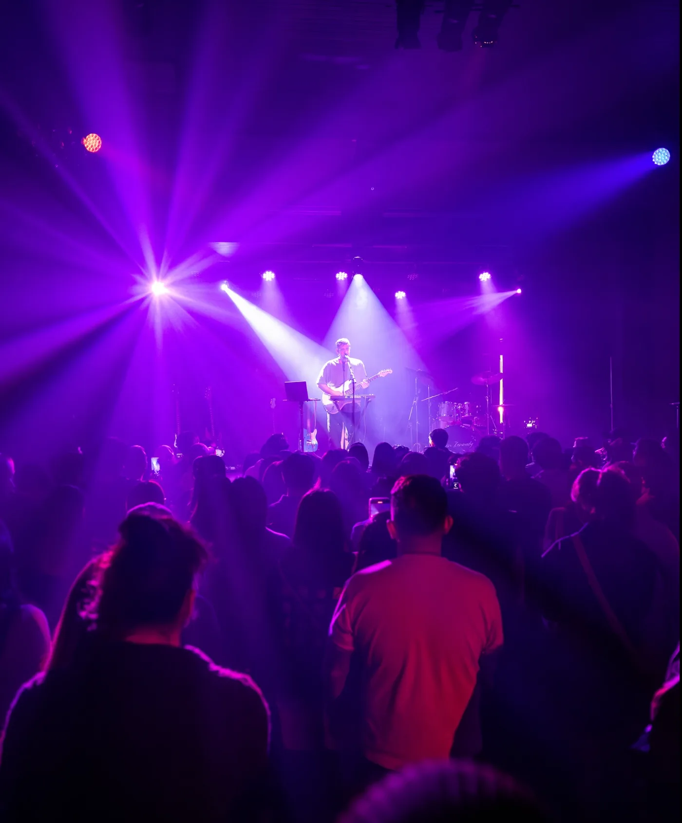 Adam Turley performing under a wash of purple stage lights with a packed crowd looking on