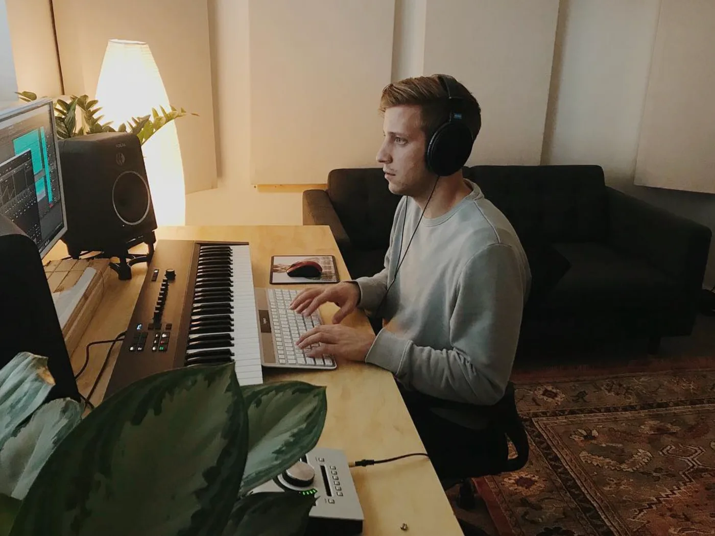 Adam Turley at his home studio desk, headphones on, mousing through a DAW next to a MIDI keyboard and studio monitor