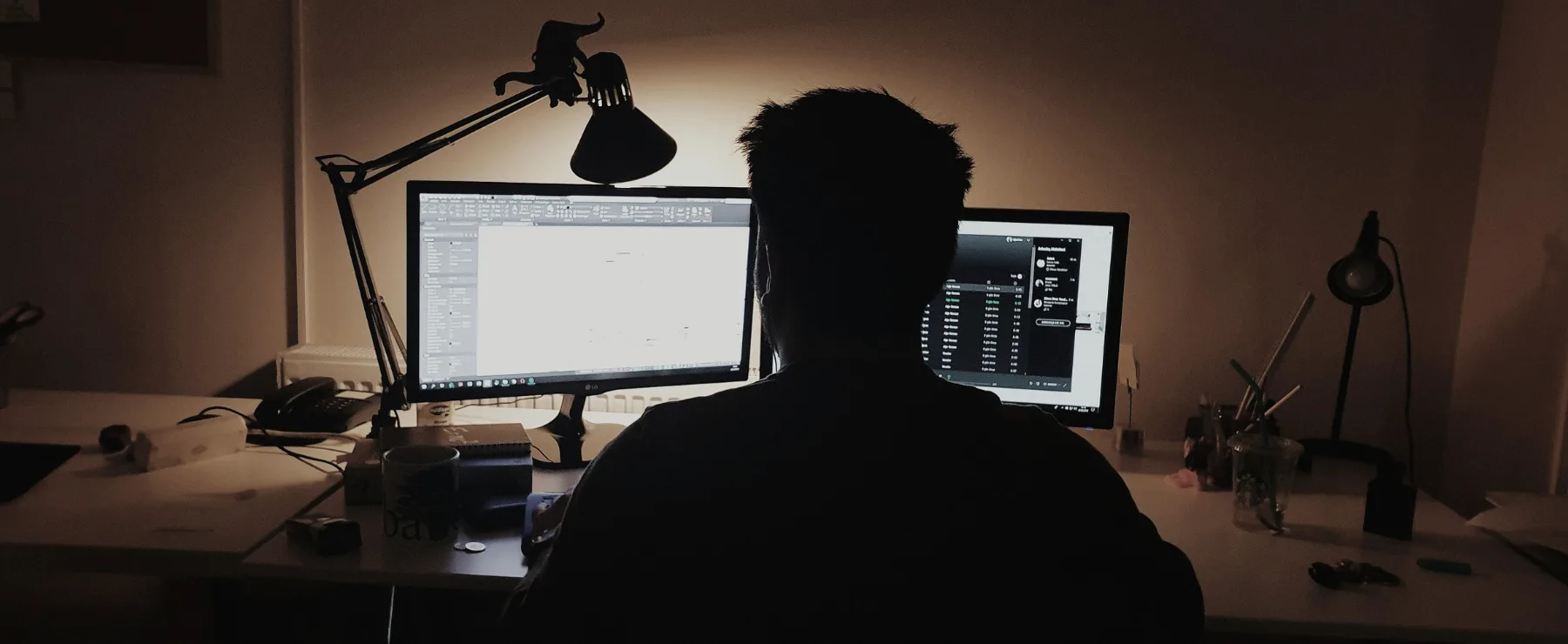 Producer working late at a dual-monitor desk in a dimly lit room