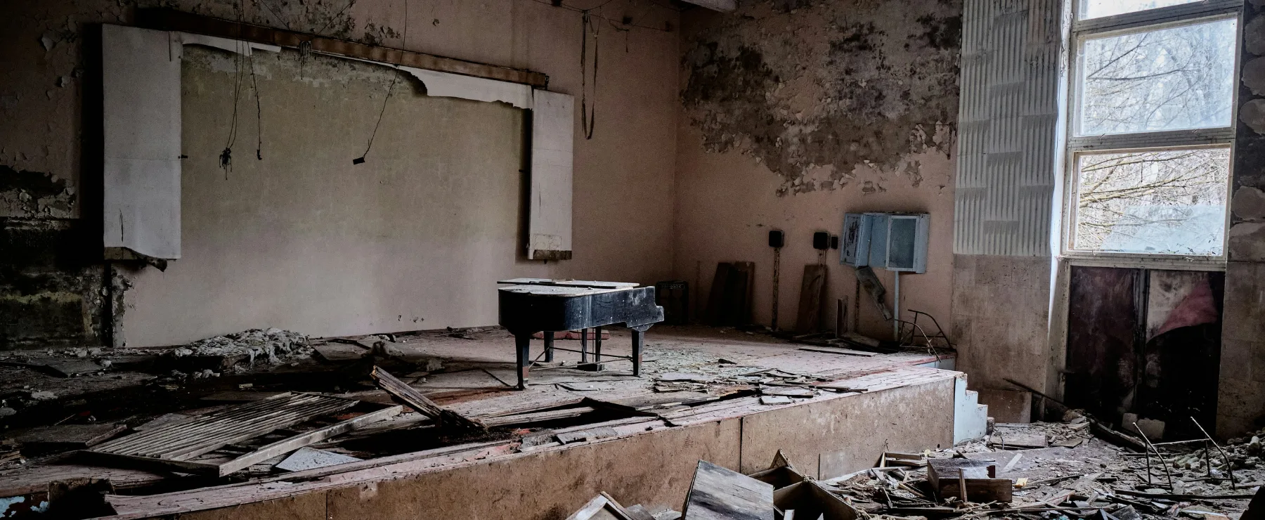 Abandoned school auditorium with a derelict grand piano on a collapsed stage