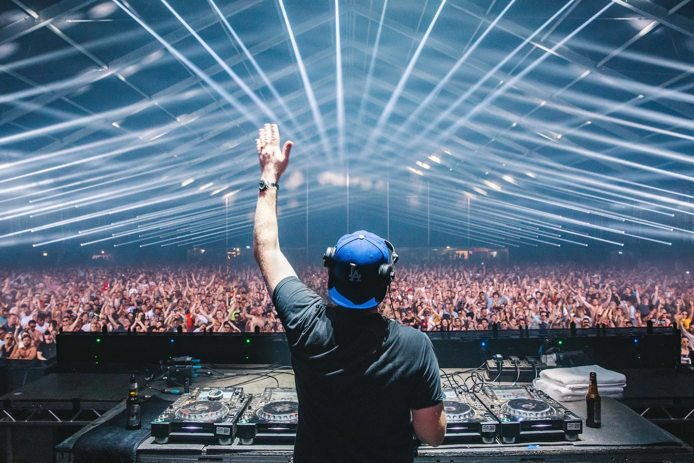 Eric Prydz behind the decks with arm raised, laser rig and festival crowd stretching into the distance