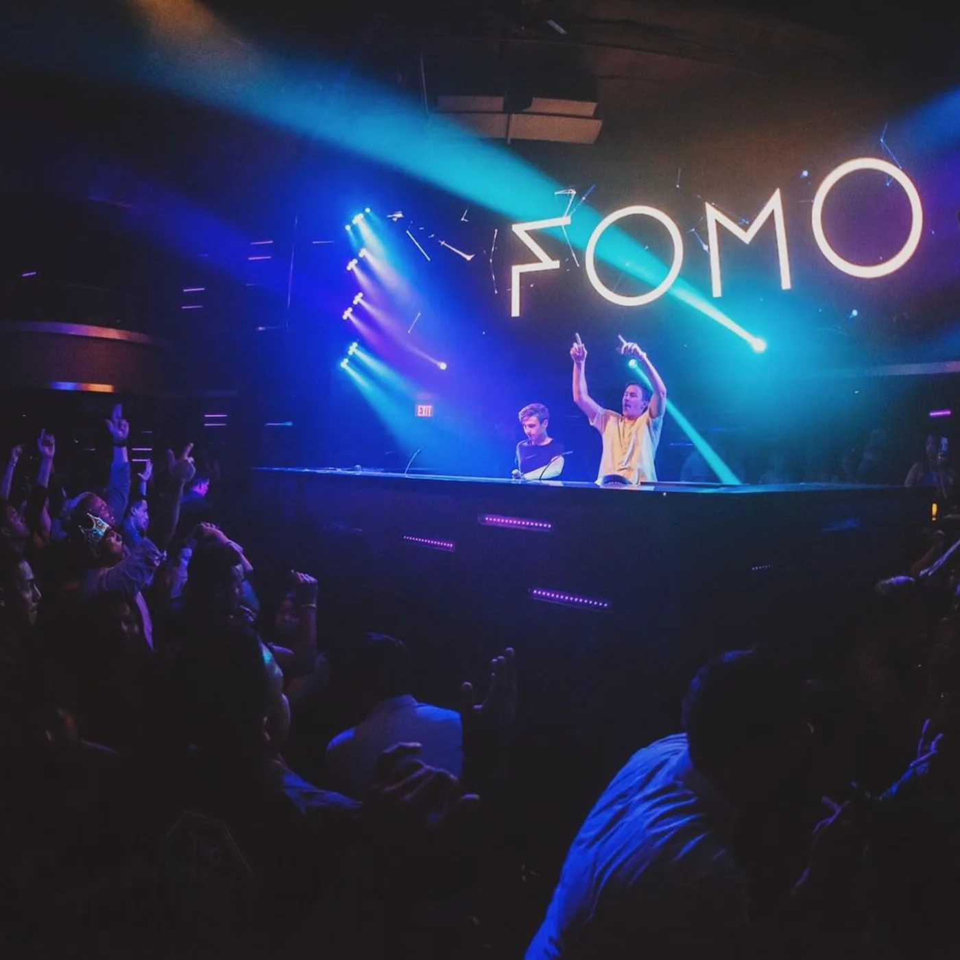 FOMO behind the decks under their logo sign, hands raised to a packed room