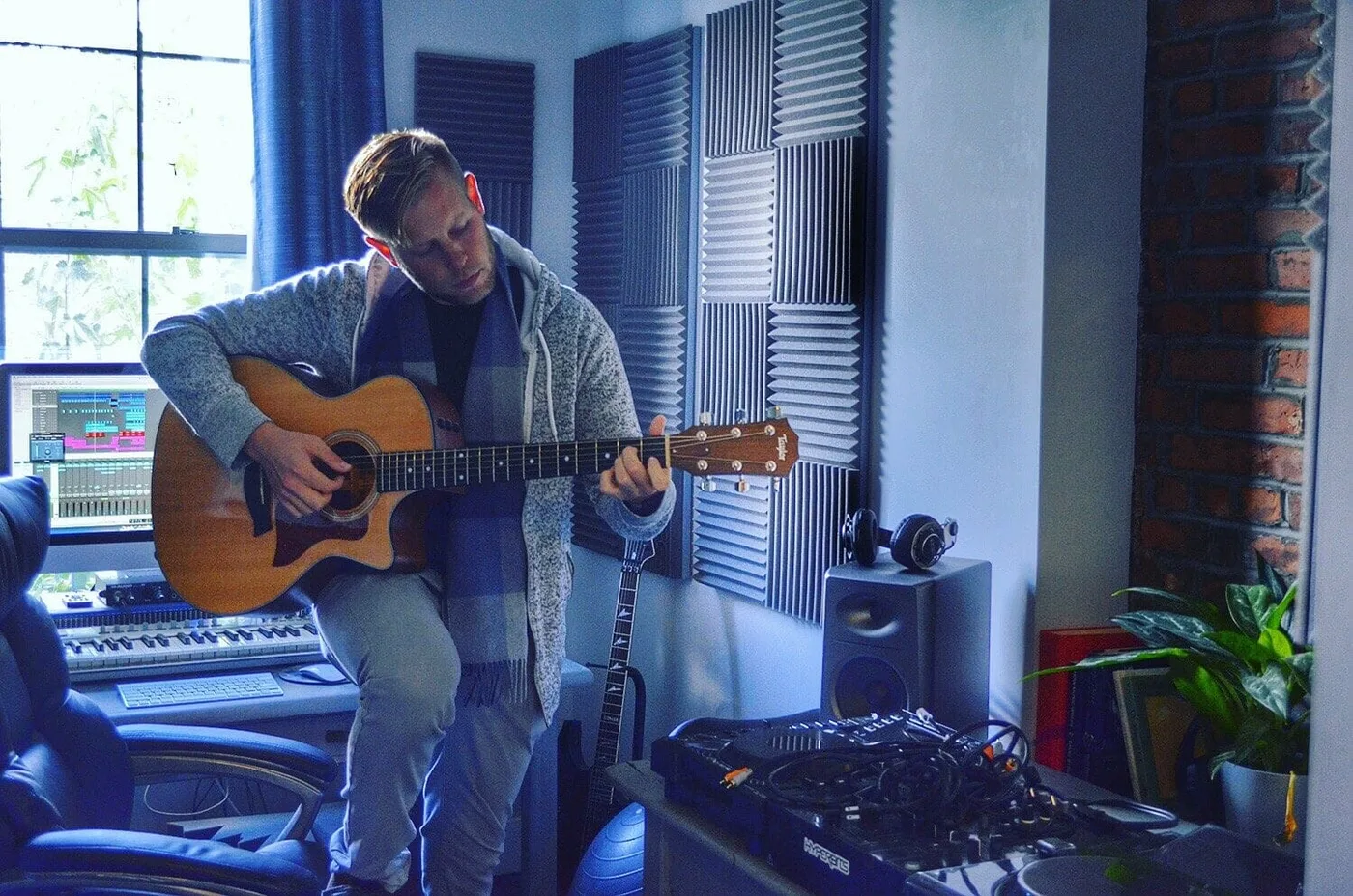 Serik playing guitar indoors wearing a scarf, Brooklyn apartment studio session