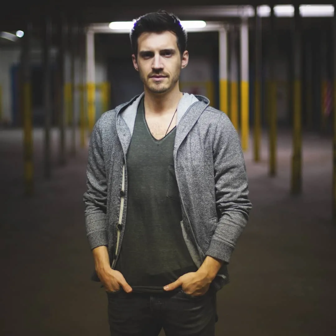 Joel Freck in a hoodie standing under warehouse lights, alt press portrait