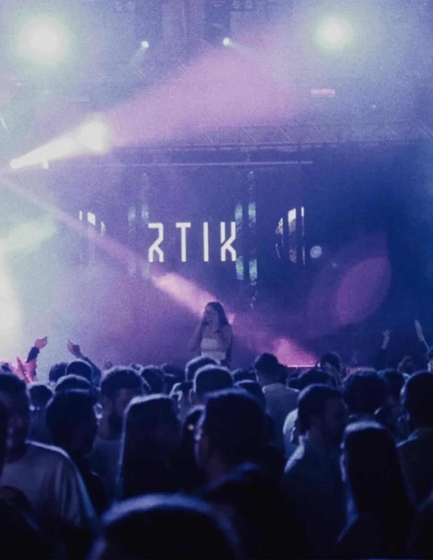 A packed crowd raising their hands under purple lights as RTIK headlines with his name on the LED backdrop