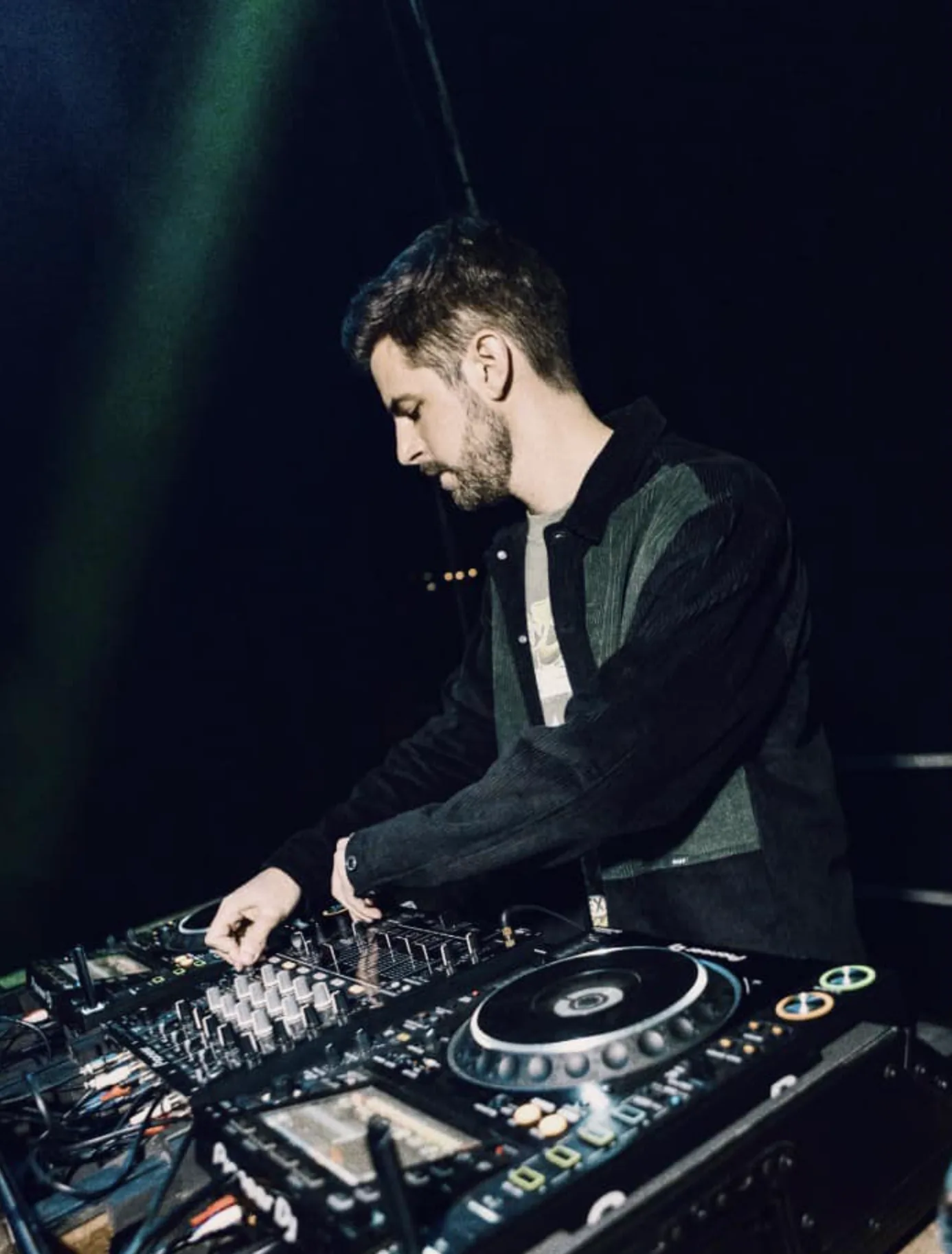RTIK behind the CDJs mid set, lit by green stage lights in a dark club