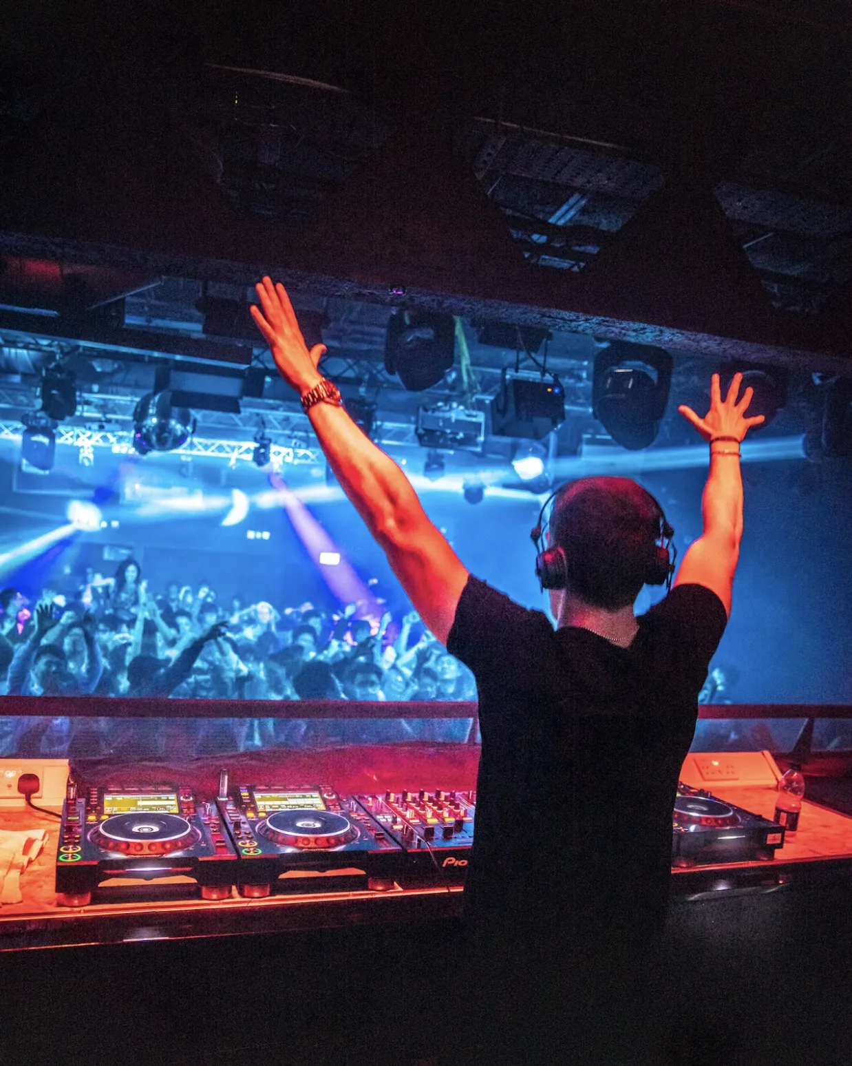 Josh Le Tissier DJing at Ministry of Sound, hands raised in front of blue stage lights